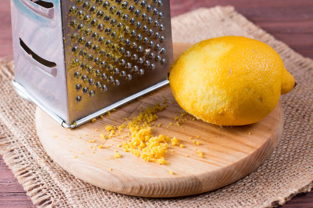 натереть кожуру и лимонную цедру на деревянном столе - grater grated peel ingredient стоковые фото и изображения