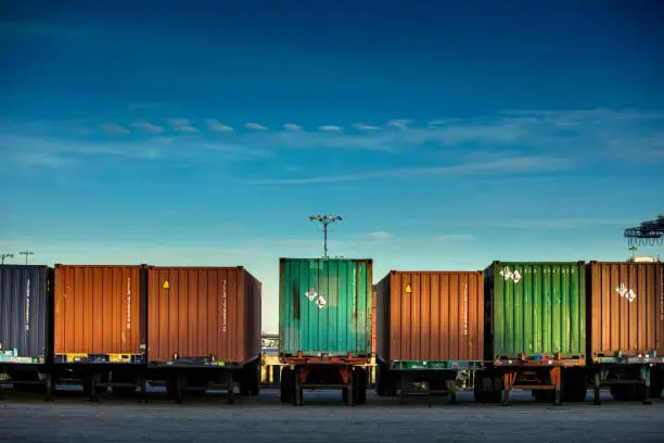 Rear view of a line of trucks loaded with differently colored shipping containers.