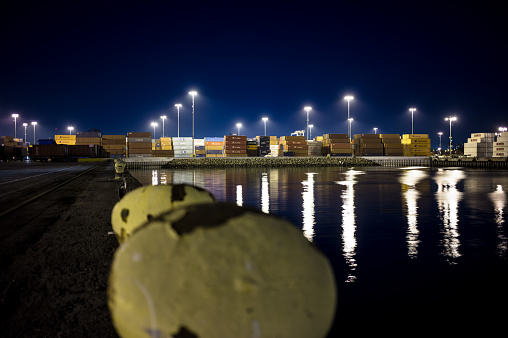 View of a shipping container yard across a channel of water in the Port of Long Beach at night.