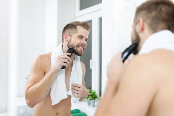 guapo hombre barbudo recorte su barba con un condensador de ajuste - barba pelo facial fotografías e imágenes de stock