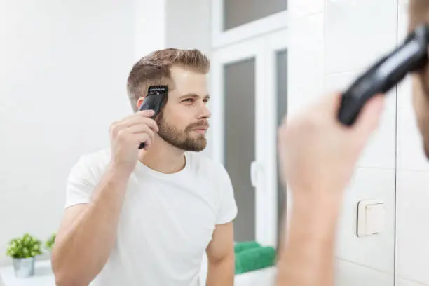 Photo of Handsome man cutting his own hair with a clipper