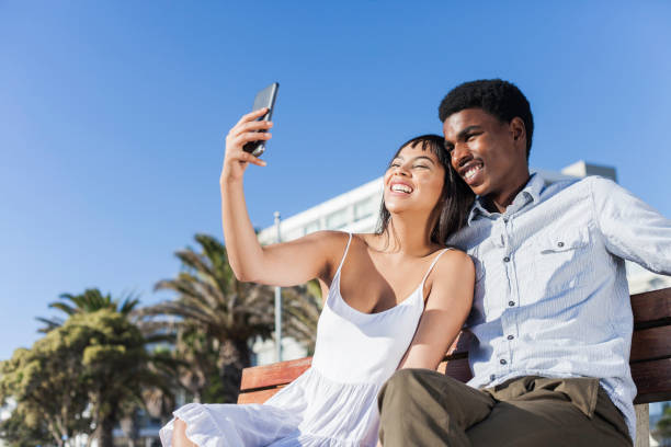 istock Young man and woman taking selfies while sitting on a bench together. 913438088