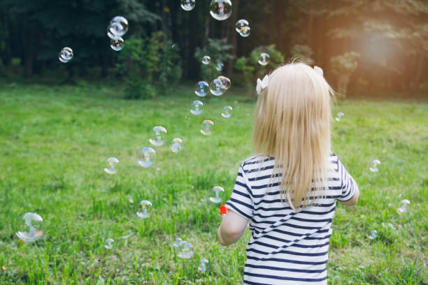istock Little girl inflate soap bubbles on the lawn 913445340