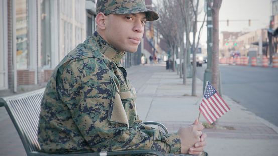 Military Man holds an American Flag in the city.
