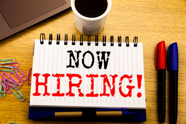istock Hand writing text caption showing Now Hiring. Business concept for Hire Recruitment written on notebook book on the wooden background in the Office with laptop coffee 913457316