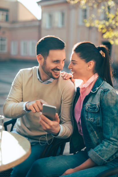 young couple surfing the net while enjoying coffee outdoors - surfing wireless vertical outdoors lifestyles imagens e fotografias de stock