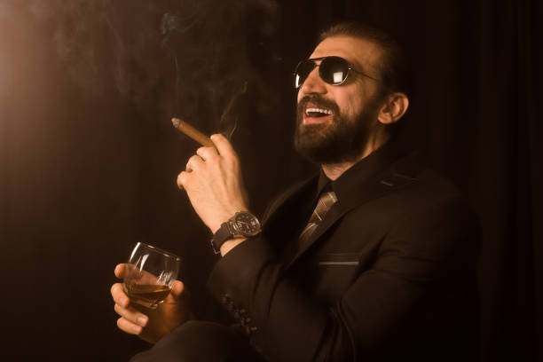 laughing elegant man in suit sepia photo The laughing elegant man or mafia boss in suit is smoking cigar and holding alcohol in hand, sepia photo, retro style. mafia boss stock pictures, royalty-free photos & images