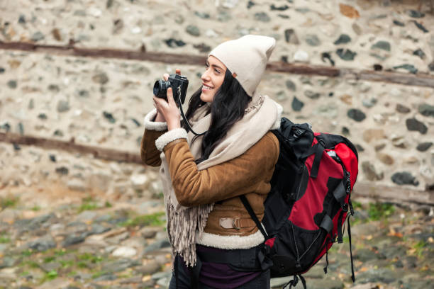 Girl tourist holding a camera and looking at him in the background of the stone building