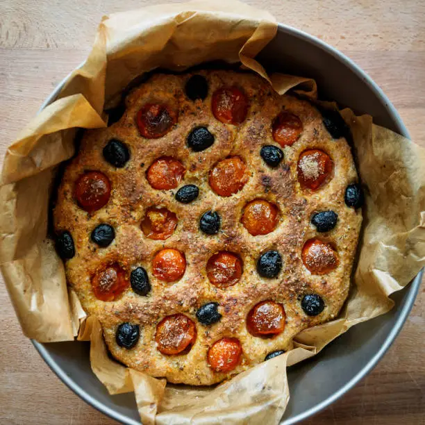 Photo of Close up of a typical Apulian focaccia in a tin tray on a wooden board.