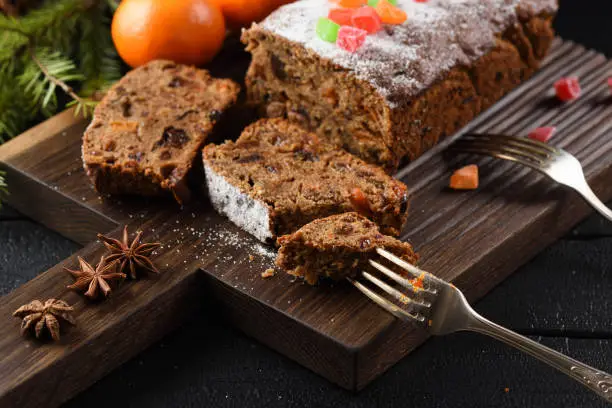 Slices of traditional English fruit cake with candied fruits served with clementines and star anise on oak board closeup