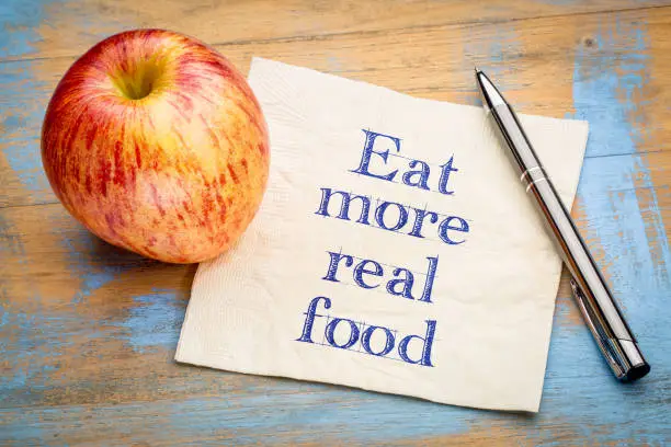 Eat more real food reminder  - handwriting on a napkin with a fresh apple