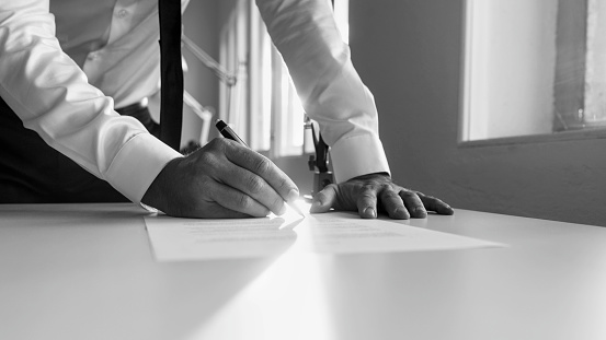 Greycale image of a man signing contract or document in the office at sunset.