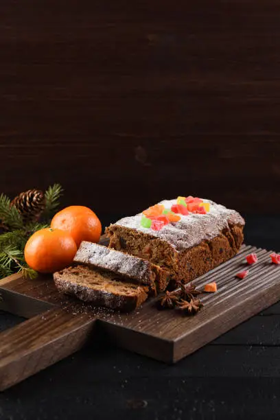 Tasty sliced fruit cake with candied fruits and clementines on dark background copy space vertical