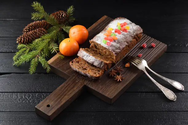 Yummy chocolate fruit cake decorated with candied fruits, clementines and fir branch on dark oak background and burnt wood