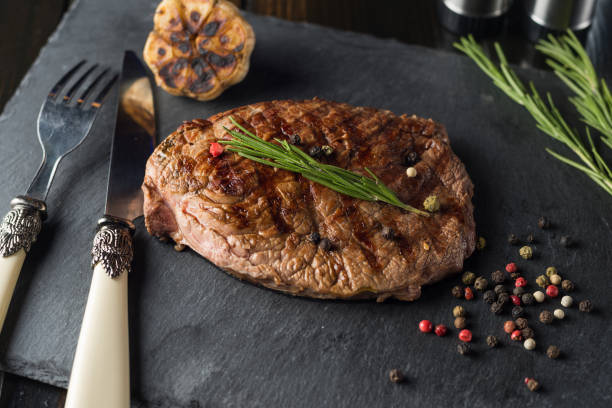 istock Grilled beef steak on stone plate over wooden table with fork and knife 913508530