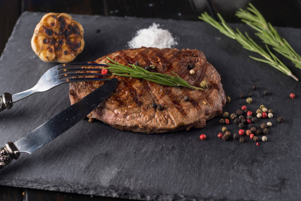 istock Grilled beef steak on stone plate over wooden table with fork and knife 913508642