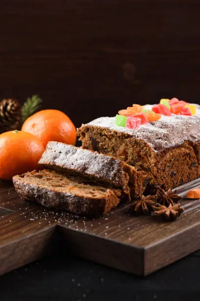Tasty English fruit cake decorated with candied fruits served with clementines on oak board copyspace closeup