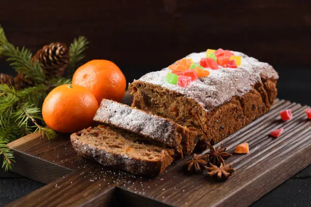 Traditional homemade chocolate fruit cake decorated with candied fruits, clementines, star anise and fir branch on carved dark oak board closeup