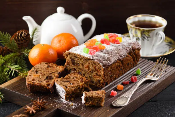 Delicious sliced fruit cake on wooden board served with tea and clementines with fir tree and cones