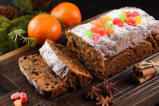 Freshly backed fruit cake with raisins, prunes and dried apricots decorated with candied fruits on dark oak board closeup