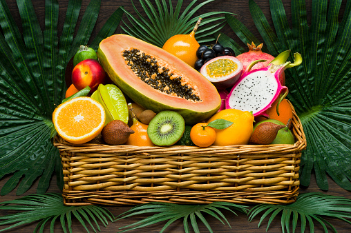Fresh Thai fruits in wicker basket on palm leaves and wooden background, healthy food, diet nutrition