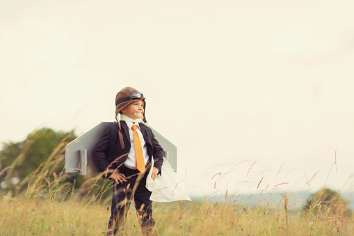 A young British Boy dressed in business suit and homemade jet pack stands with confidence in a field atop a hill in Gloucestershire, United Kingdom. He looks into the sky waiting to take his business to new successes.