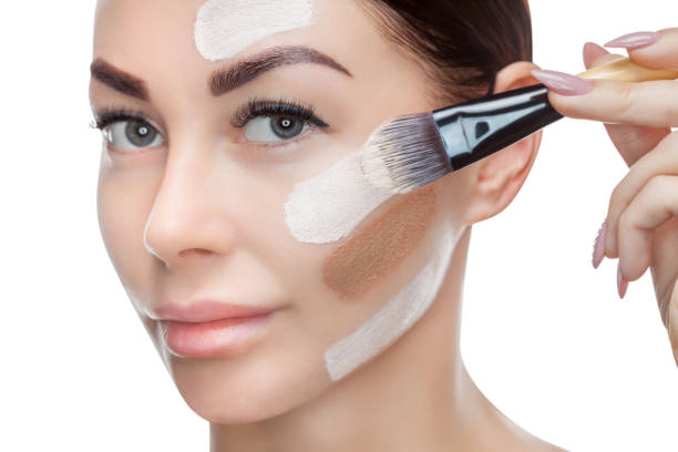 istock Beautiful young woman is applying a foundation on her face with a brush 913542786