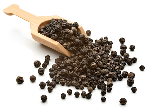 Black pepper grains in a serving scoop. 