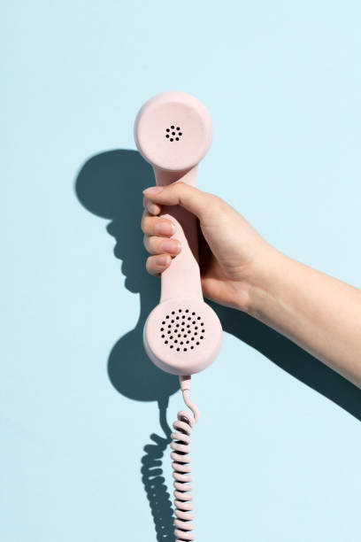 Woman's hand holding a pastel telephone Woman's hand holding a pastel telephone on a blue background. Telecommunication. telephone receiver stock pictures, royalty-free photos & images