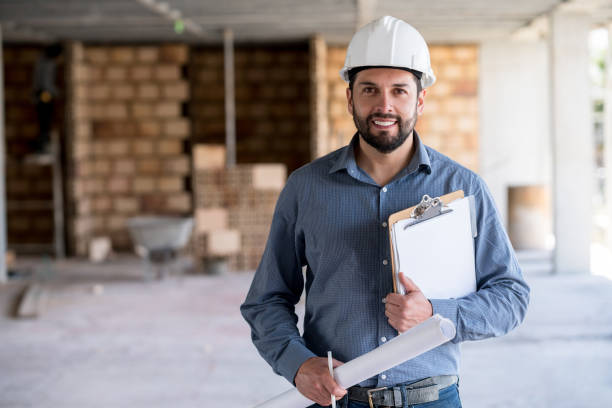 Portrait of an engineer holding a blueprint at a construction site Portrait of an engineer holding a blueprint at a construction site while wearing a helmet and looking at the camera smiling building contractor stock pictures, royalty-free photos & images
