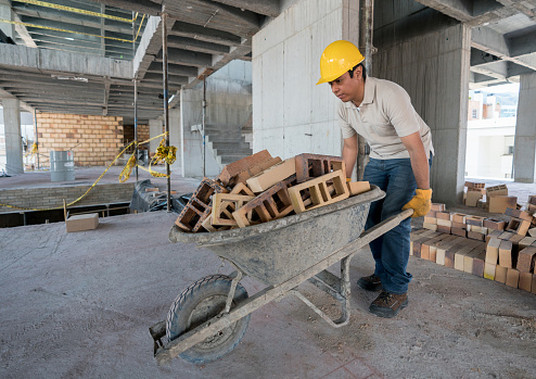 Construction worker carrying bricks on a wheelbarrow at a building site