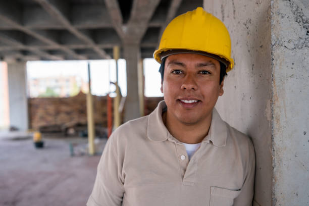 Portrait of a construction worker looking at the camera smiling wearing a helmet while leaning on a wall