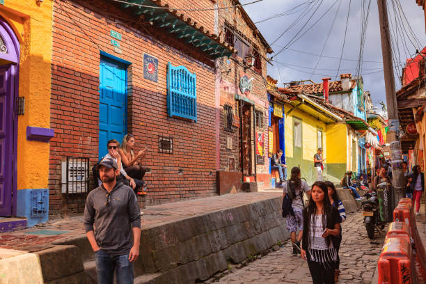 Bogotá, Colombia - Local Colombians On The Cobblestoned Calle del Embudo, In The Historic La Candelaria District of The Andean Capital City Bogotá, Colombia - May 28, 2017: Local Colombian people and a few tourists walk up the narrow Calle del Embudo which gets its name from its shape. The English translation of the name would be, "Funnel Street." It is one of the most colorful streets in the historic La Candelaria district of Bogotá, the Andean capital city of the South American country of Colombia. Constructed over 450 years ago, the street leads to the Chorro de Quevedo, the plaza where it is believed the Spanish Conquistador, Gonzalo Jiménez de Quesada founded the city in 1538. Many street facing walls in this area are painted with either street art or the legends of the pre-Colombian era, in the vibrant colours of Colombia. Photo shot in the afternoon sunlight; horizontal format. Camera: Canon EOS 5D MII. Lens EF 24-70 mm F2.8L USM. calle del embudo stock pictures, royalty-free photos & images