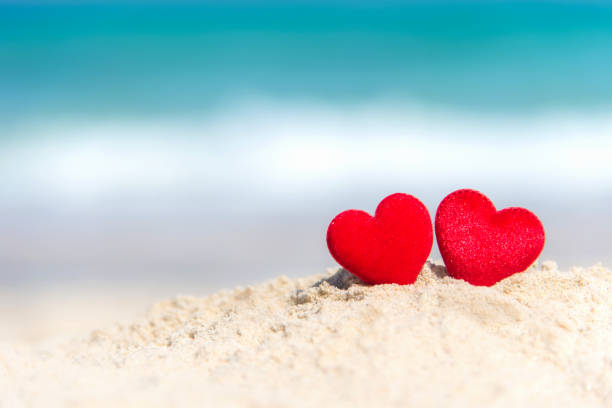 istock Valentine Concept.  Two red hearts on the sand summer beach, blue background. 913613382