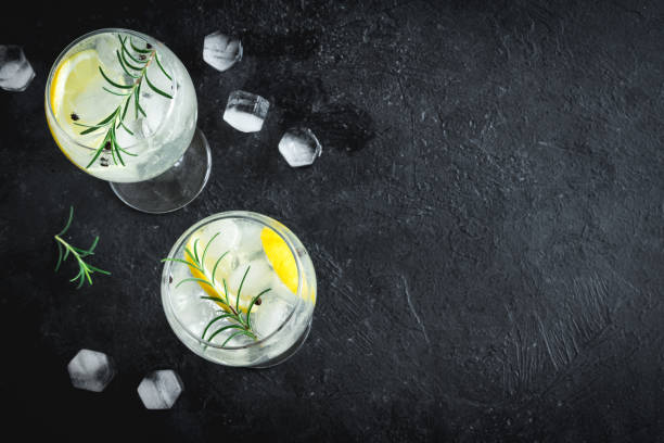 gin tonic cocktail Alcohol drink (gin tonic cocktail) with lemon, rosemary and ice on rustic black stone table, copy space, top view. Iced drink with lemon and herbs. vodka photos stock pictures, royalty-free photos & images