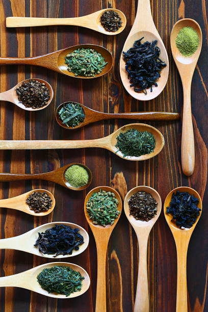 varie foglie di tè assortite in cucchiai di legno di diversa forma, colpo in testa su tavolo di legno - tea leaves chinese tea green tea leaf foto e immagini stock