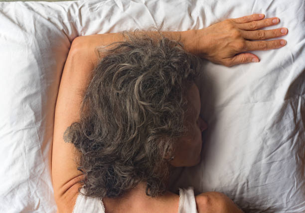 Back view of middle aged woman sleeping on pillow from above High angle close up  view of middle aged woman sleeping face down on pillow with arm overhead (selective focus) face down stock pictures, royalty-free photos & images