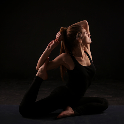 Young woman practicing yoga in Royal Pigeon pose. About 25 years old, Caucasian blonde.