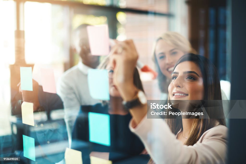 Unearthing brilliant new ideas for business Shot of a group of businesspeople arranging sticky notes on a glass wall in a modern office Marketing Stock Photo