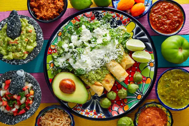 Green enchiladas Mexican food with guacamole and sauces on colorful table