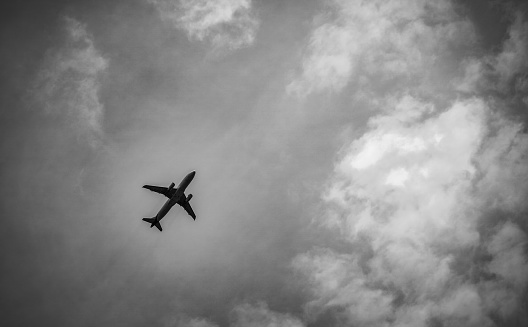 Black and white scene of International airline after take off on grey sky and white clouds.