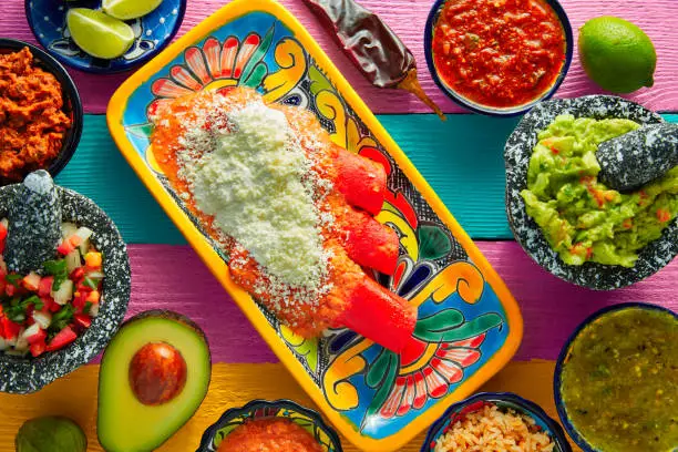 Red enchiladas Mexican food with guacamole and sauces on colorful table