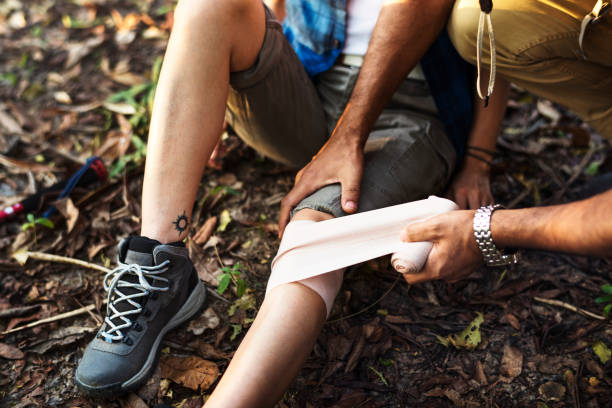 Man putting bandage on his partner&#39;s knee in the jungle stock photo