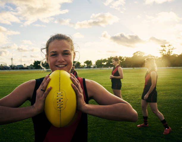 I like to play rough Shot of a young woman holding a football on a field with her team in the background rugby players stock pictures, royalty-free photos & images