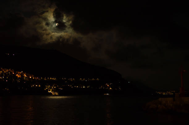 Moon in the Clouds creating Moonbeams with a boat at anchor in the water.