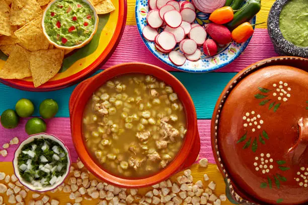 Green Pozole verde with blanco mote corn and ingredients on colorful table