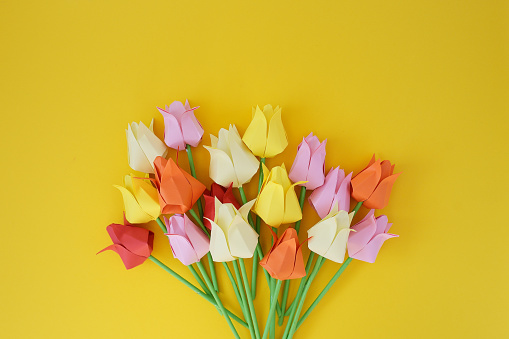 Tulips of origami from multi-colored  paper on a yellow background
