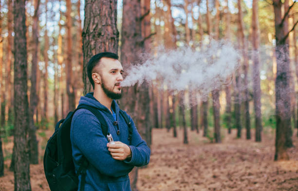 istock Casual men with beard vaping an electronic cigarette outdoors in forest. Safe smoking. 913683614