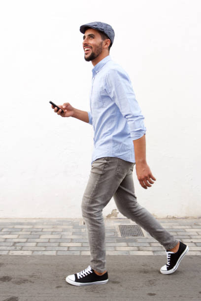 istock Full length smiling man walking with cellphone against white wall 913688934
