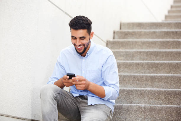 young arabic man sitting on steps and looking at mobile phon Portrait of young arabic man sitting on steps and looking at mobile phone north african ethnicity stock pictures, royalty-free photos & images